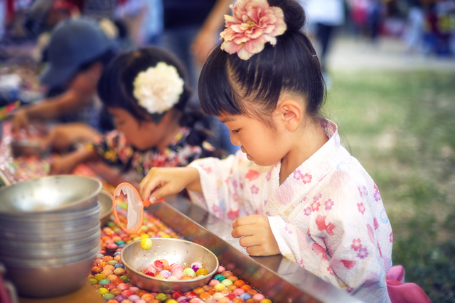 Young Japanese girl scooping balls out of a bowl with a broken net.