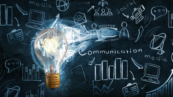 A lit lightbulb lighting up the chalkboard covered in science communication lingo and drawings.