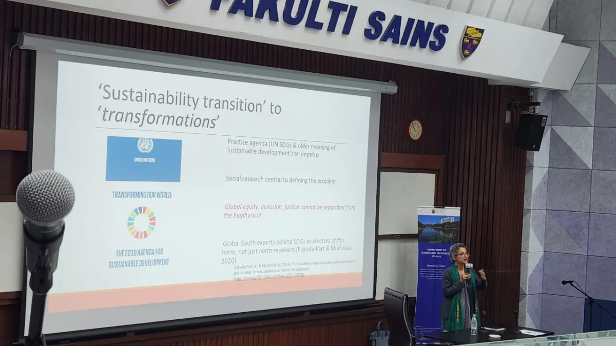 A woman on a stage presenting with a large powerpoint in a university. 