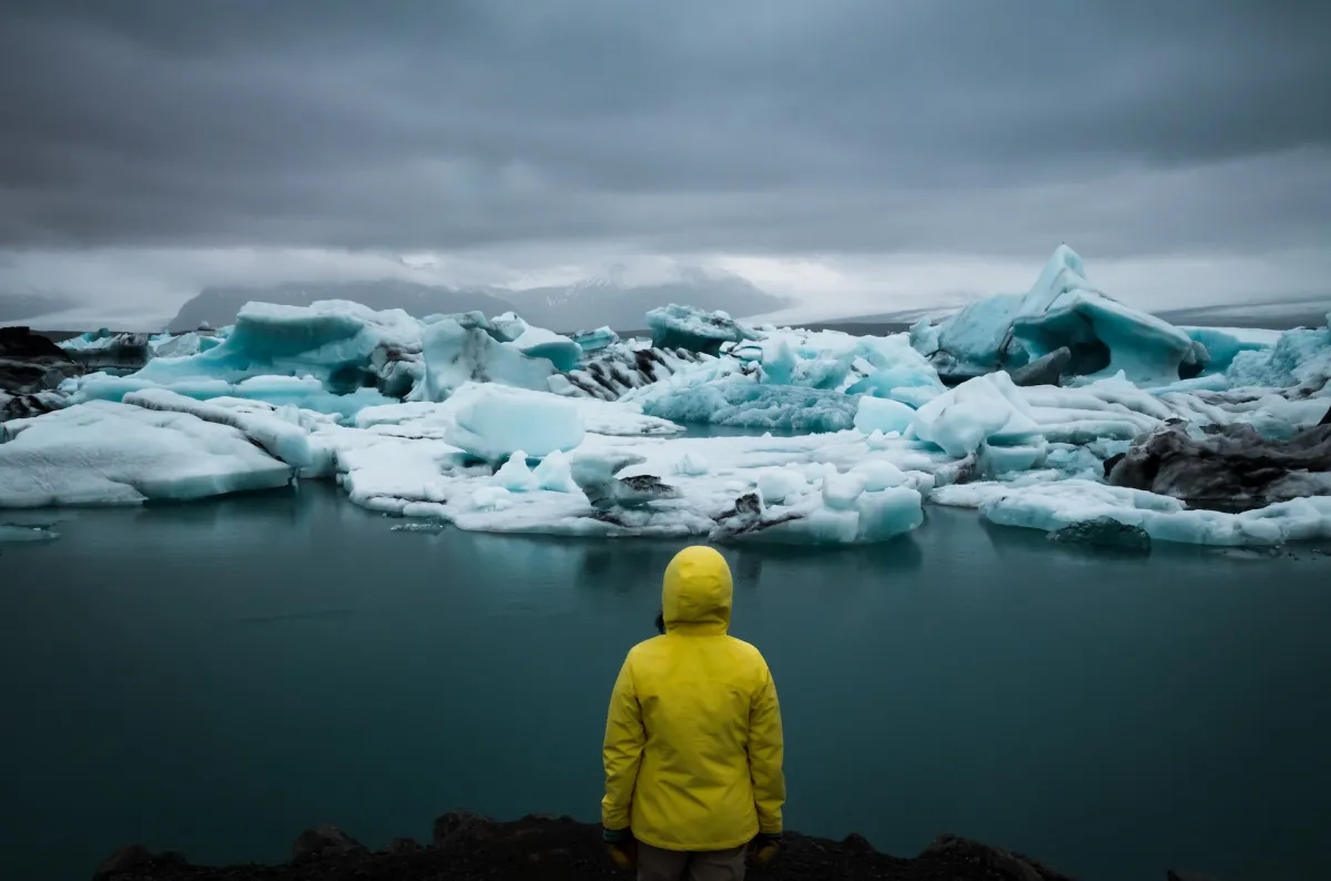 A person in a yellow coat looking at large floating pieces of ice and broken icebergs.
