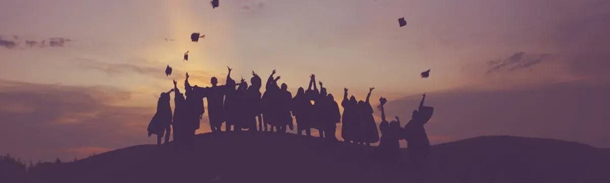 Group of people on hillside throwing their graduation caps in the air.