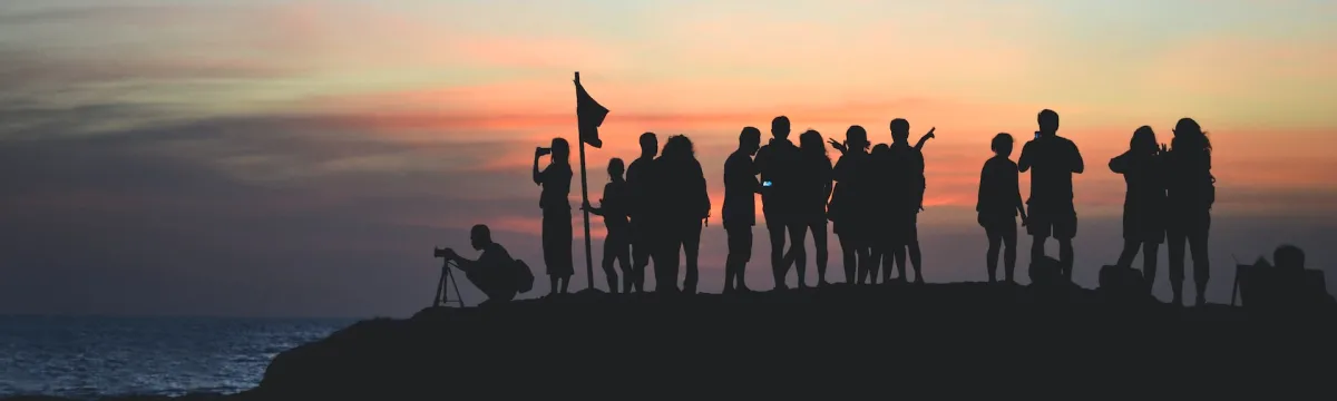 A group of 15 people on the edge of a cliff staring out at the sunset.