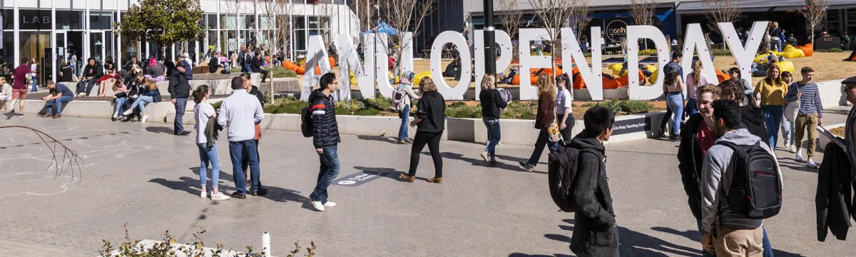 Image of people walking down a bring road with block standing letters spelling out ANU OPEN DAY.