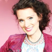 Headshot of woman with pink leather jacket and pink background.