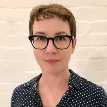 Headshot of a woman in glass in front of a white brick wall.