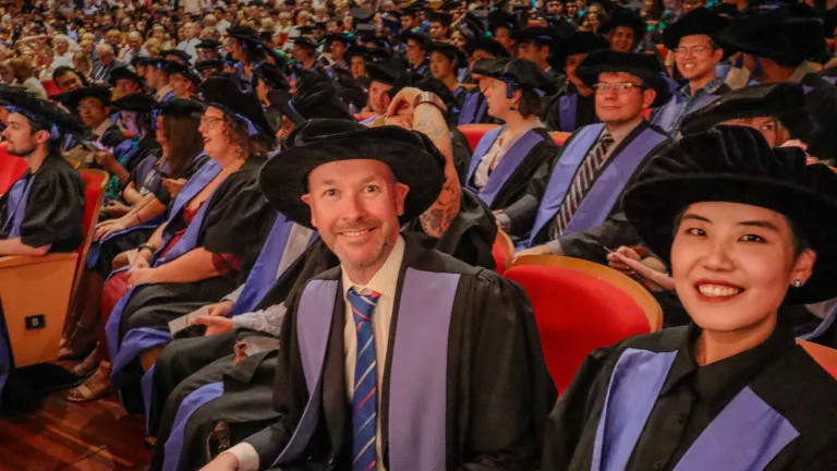 A man and a woman smiling in their graduation cap and gown.