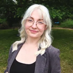 Headshot of white women, blonde hair, and glasses wearing a black tank-top and gray jacket