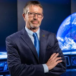 Man in a suit with hands crossed an a graphic display of planet earth in the background.