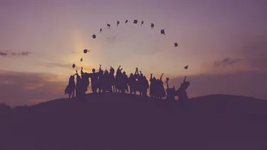 Group of people on hillside throwing their graduation caps in the air.